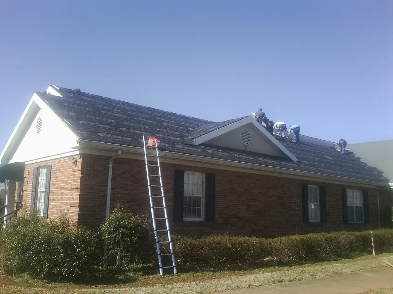 Crew tearing shingles off a brick ranch roof with a ladder set — Metal Roof Repair work by our crew in Cottekill