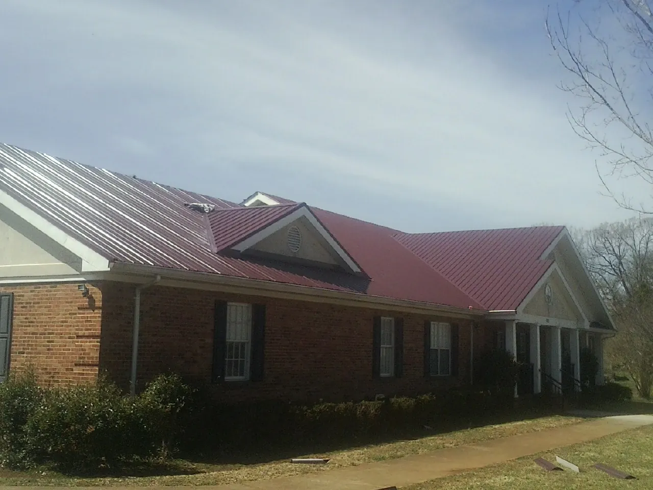 Red metal roof with gabled entries on a long brick building, from a Hail Damage Roof Repair job in Cottekill