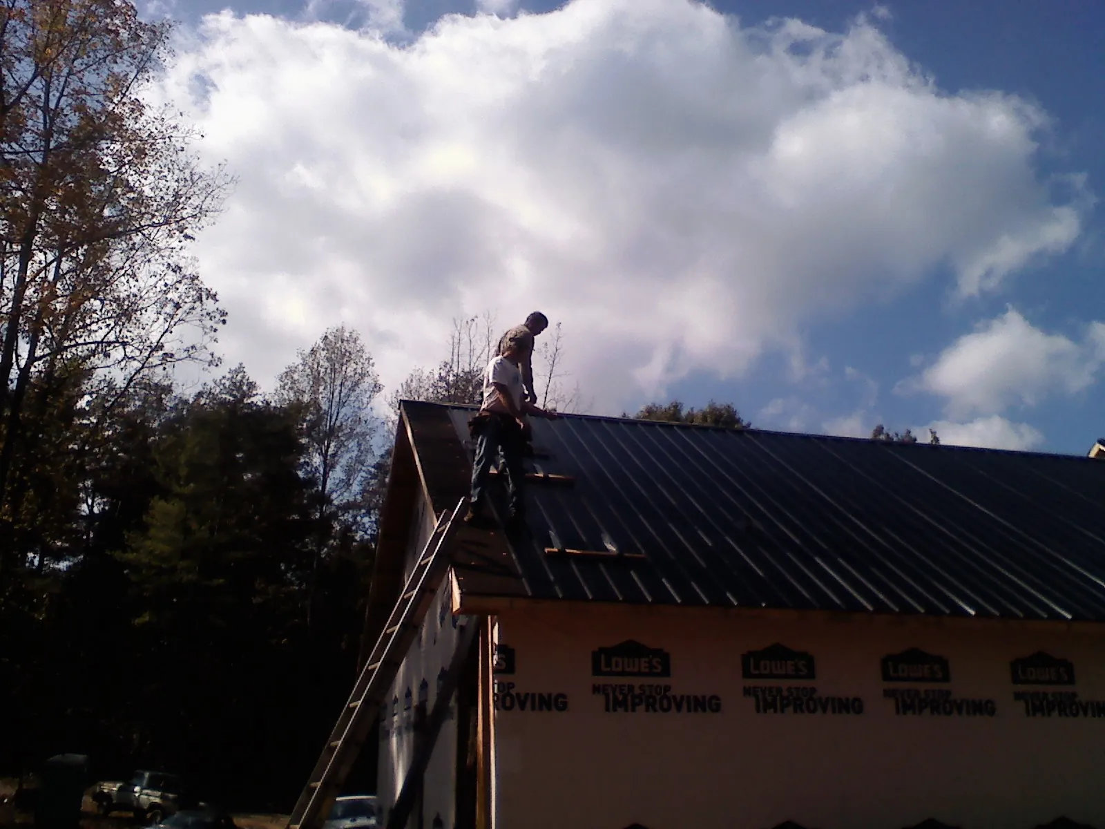 Roofer fastening dark metal panels high against a cloudy sky, from a Roof Inspection job in Cottekill